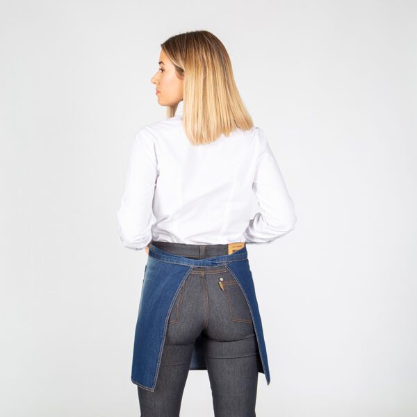 Delantal corto denim con efecto lavado y desgastado, mostrando sus tres bolsillos frontales.