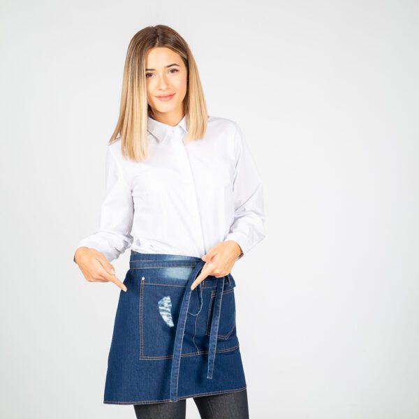 Delantal corto denim con efecto lavado y desgastado, mostrando sus tres bolsillos frontales.